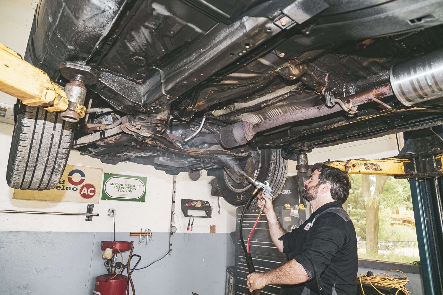 An Auto Solve technician applying rustproofing to a vehicle on the shop lift