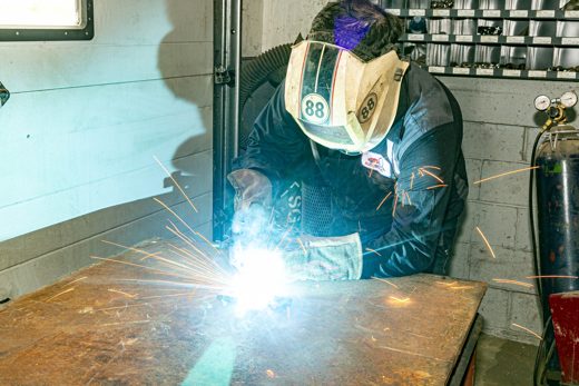 Auto Solve technician welding a fabricated exhaust section, sparks flying