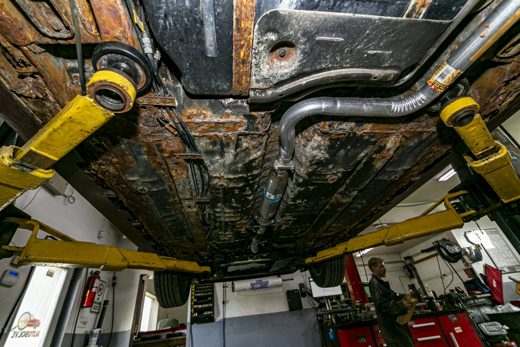 Rusty vehicle undercarriage exhaust system on the lift — pipes, muffler, and hangers exposed to Ontario road salt